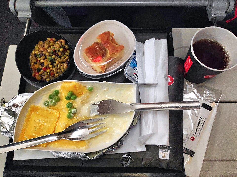 Image shows airline food - a lunch meal in 2024 served onboard a long distance flight on Turkish Airlines economy class. Ravioli, mung bean salad, cake and coffee with real metal cutlery