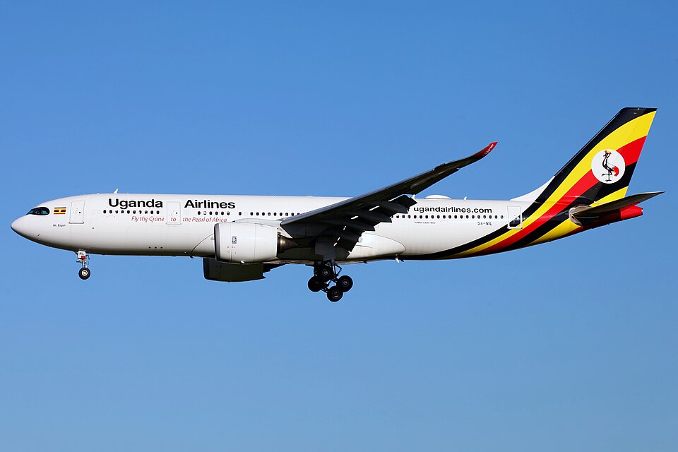 A Uganda Airlines Airbus A330-800neo widebody passenger plane (registration 5X-NIL) flies mid-air with landing gear down against a clear blue sky background.