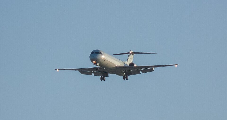 A white Bombardier CRJ regional jet approaching head-on for landing with landing gear down and navigation lights illuminated, centered against a clear light blue sky.