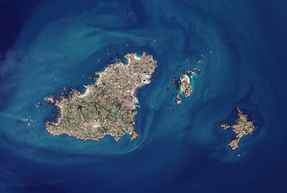 Space view from the island of Guernsey. The sea is dark blue further from the island and gets progressively lighter closer to the shore.