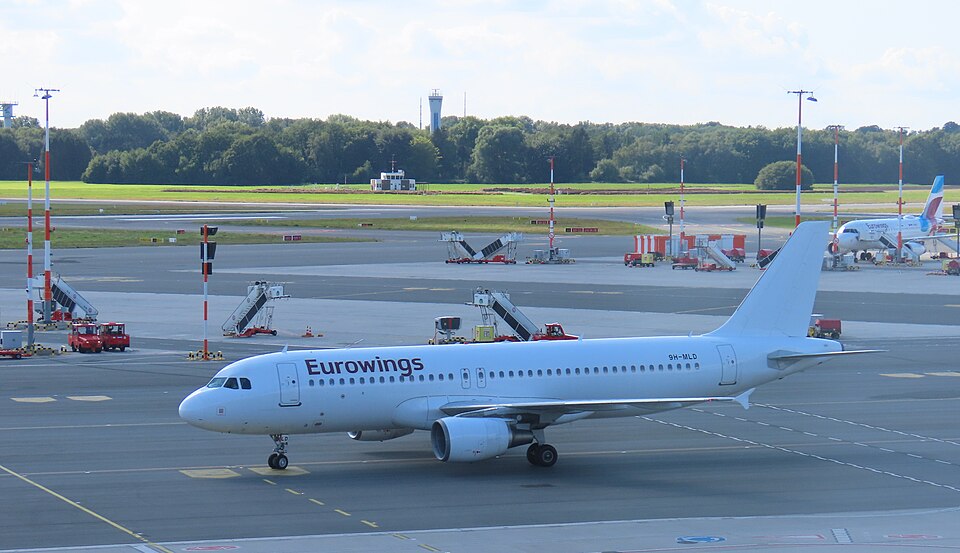 A white Eurowings Airbus A320-214 commercial jet, registered as 9H-MLD, parked on an airport apron during daytime operations.