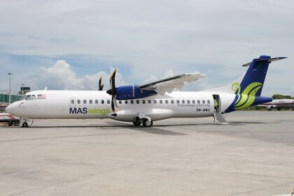 An ATR 72-500 twin-engine turboprop passenger airliner, operated by MASwings with tail number 9M-MWA, sits parked on the airport tarmac on a bright, partly cloudy day.