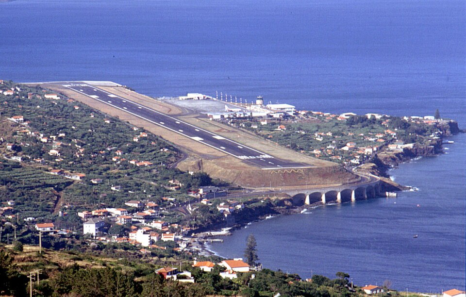 Aerial view of Madeira Airport's landing strip in the 1990s. The image has a vintage tint and mostly shows the runway and the sea surrounding it. 