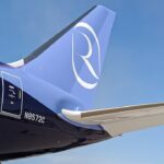 A close-up view of the tail section of a Riyadh Air Boeing 787 aircraft against a clear blue sky. The livery features a gradient from dark indigo purple on the fuselage to light periwinkle blue on the vertical stabilizer, which displays the airline's distinctive white stylized "R" logo. The registration number "N8572C" is visible on the rear fuselage near a service door, and the aircraft's horizontal stabiliser extends into the frame.