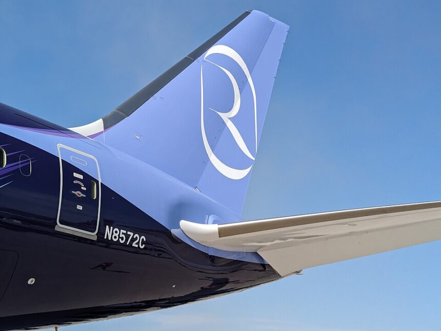 A close-up view of the tail section of a Riyadh Air Boeing 787 aircraft against a clear blue sky. The livery features a gradient from dark indigo purple on the fuselage to light periwinkle blue on the vertical stabilizer, which displays the airline's distinctive white stylized "R" logo. The registration number "N8572C" is visible on the rear fuselage near a service door, and the aircraft's horizontal stabiliser extends into the frame.