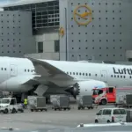 A Lufthansa Boeing 787-9 Dreamliner resting on its nose at Frankfurt Airport after a landing gear collapse with the aircraft positioned in front of a terminal building