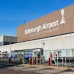 An exterior shot of Edinburgh Airport. Bus stops and people seen walking outside.