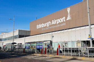 An exterior shot of Edinburgh Airport. Bus stops and people seen walking outside.