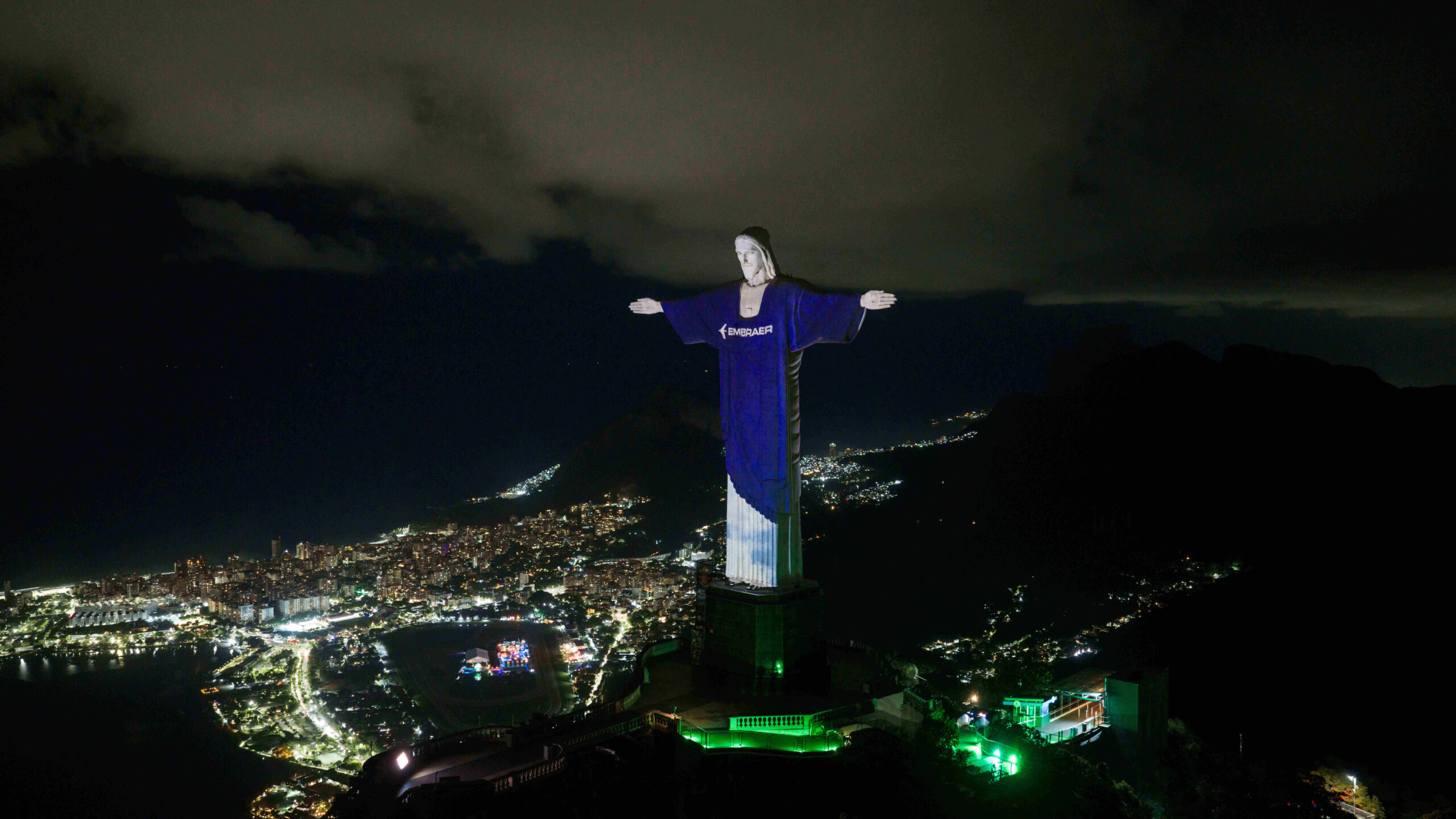 Image shows the Christ the Redeemer monument in Rio de Janeiro, Brazil, lit up at night with Embraer logo projected onto the statue.