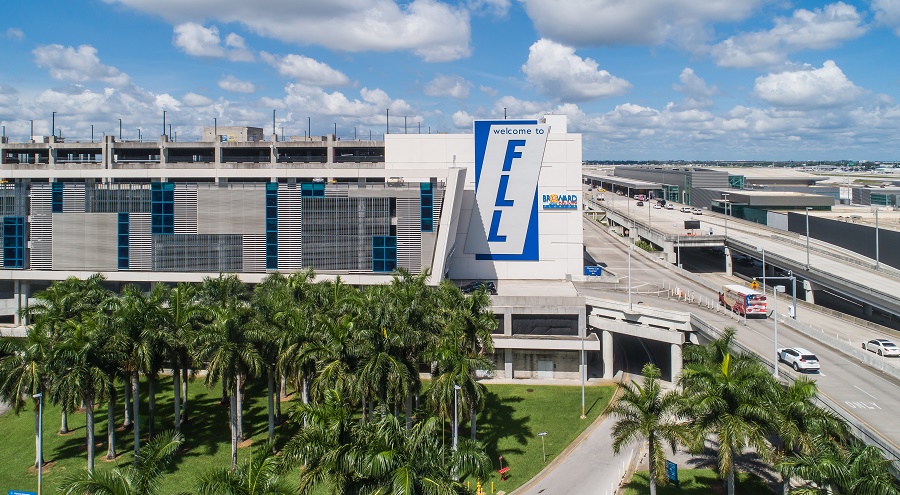 entrance to FLL with the welcome to FLL sign, palm trees and cars driving alongside airport entrance