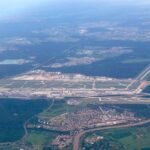 An aerial shot of Frankfurt International Airport. Surrounding trees and greenery can be seen either side of the runway and buildings.
