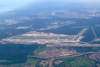 An aerial shot of Frankfurt International Airport. Surrounding trees and greenery can be seen either side of the runway and buildings.