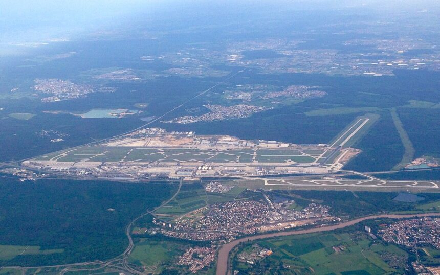 An aerial shot of Frankfurt International Airport. Surrounding trees and greenery can be seen either side of the runway and buildings.