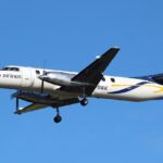 A Sharp Airlines Fairchild SA227-DC Metro 23 flying under a blue sky. The aircraft's livery is mostly white with a dark blue tail with yellow accents.