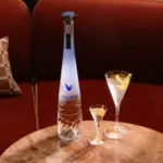 Bottle of grey goose vodka on a table alongside the small and large versions of the dry martini.