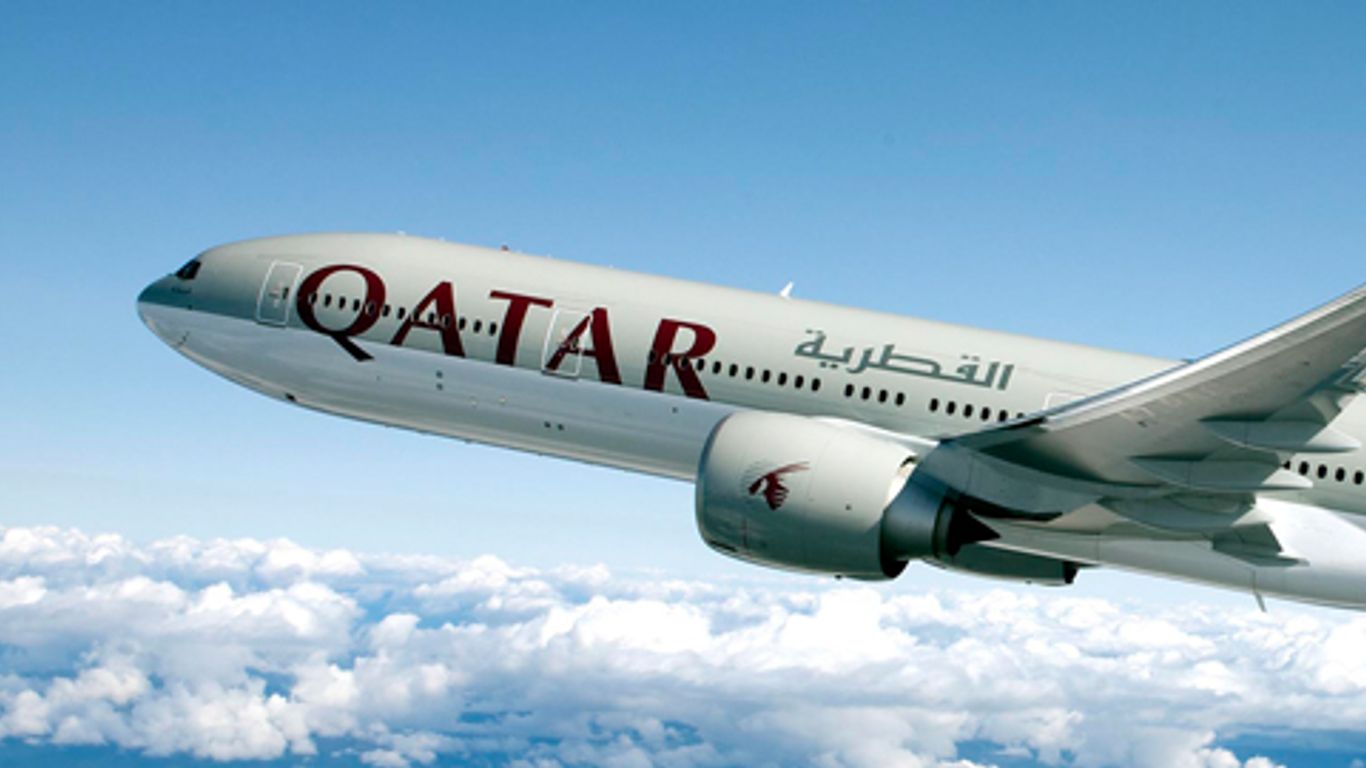 A Qatar Airways plane flying over a layer of cloud.