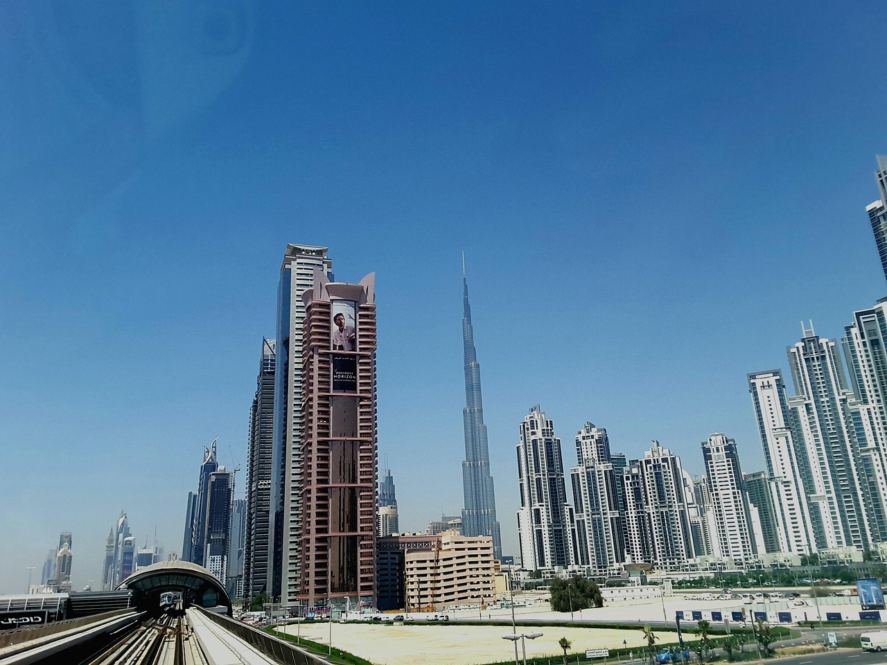 A picture of the Dubai skyline, showing the Burj Khalifa, in front of a clear blue sky, taken from a railway track.