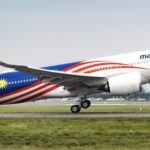 A Malaysia airlines Airbus A330 jet taking off from an airport runway in front of a field of grass.
