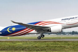 A Malaysia airlines Airbus A330 jet taking off from an airport runway in front of a field of grass.