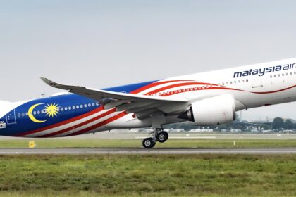 A Malaysia airlines Airbus A330 jet taking off from an airport runway in front of a field of grass.