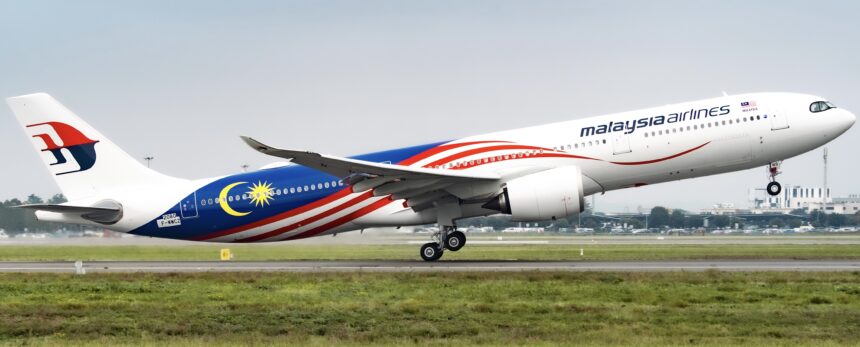 A Malaysia airlines Airbus A330 jet taking off from an airport runway in front of a field of grass.