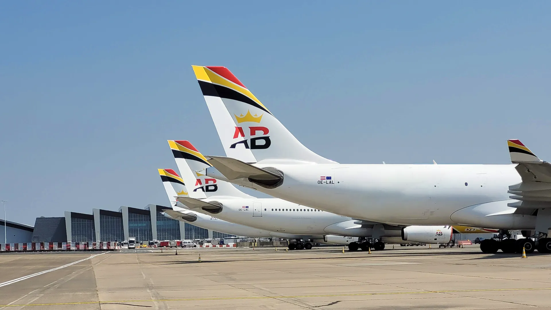The tails of three Air Belgium jets on a runway, in front of a clear sky.