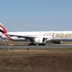An Emirates Boeing 777 jet on a runway in front of a clear blue sky.