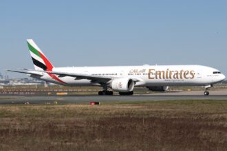 An Emirates Boeing 777 jet on a runway in front of a clear blue sky.