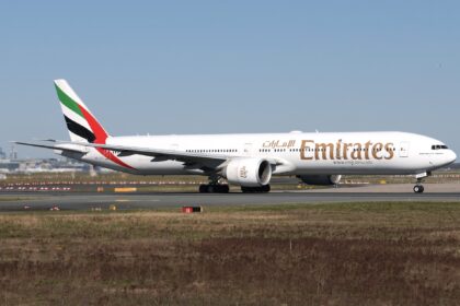 An Emirates Boeing 777 jet on a runway in front of a clear blue sky.