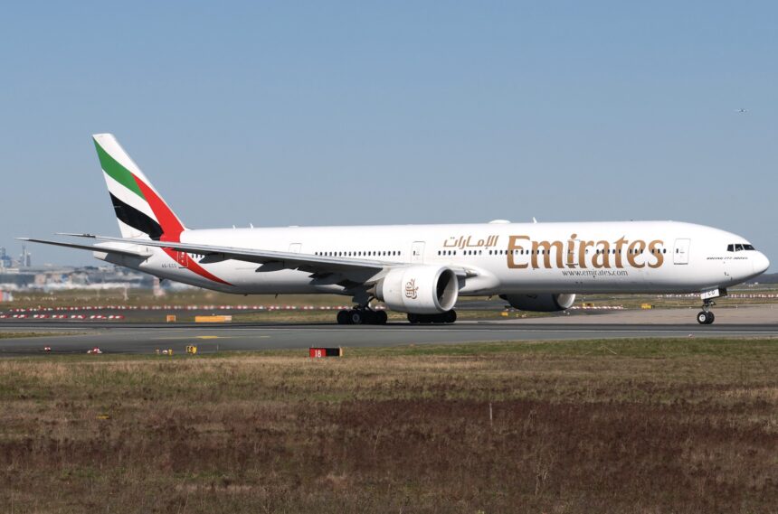 An Emirates Boeing 777 jet on a runway in front of a clear blue sky.