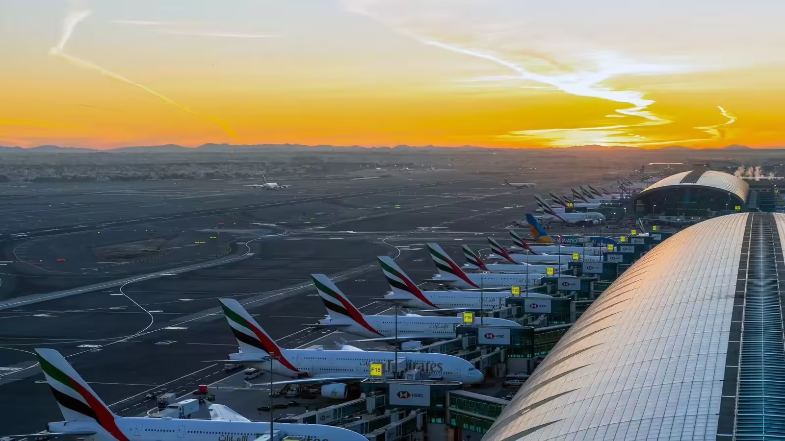 A sunset over DXB, showing a row of Emirates jets next to a terminal.