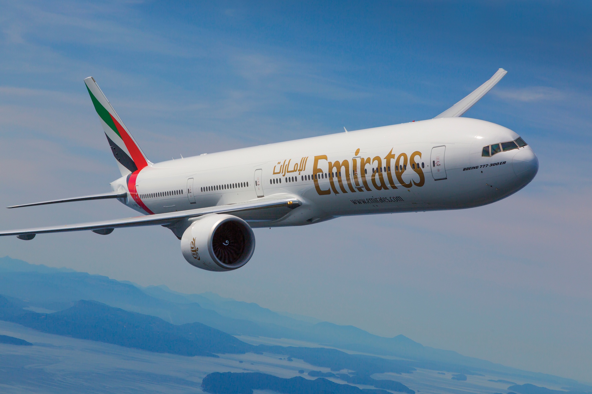 An Emirates jet turning to the right in front of a clear blue sky.