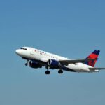 A Delta Air Lines Airbus A319 flying upwards in front of a clear blue sky.