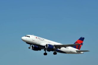 A Delta Air Lines Airbus A319 flying upwards in front of a clear blue sky.
