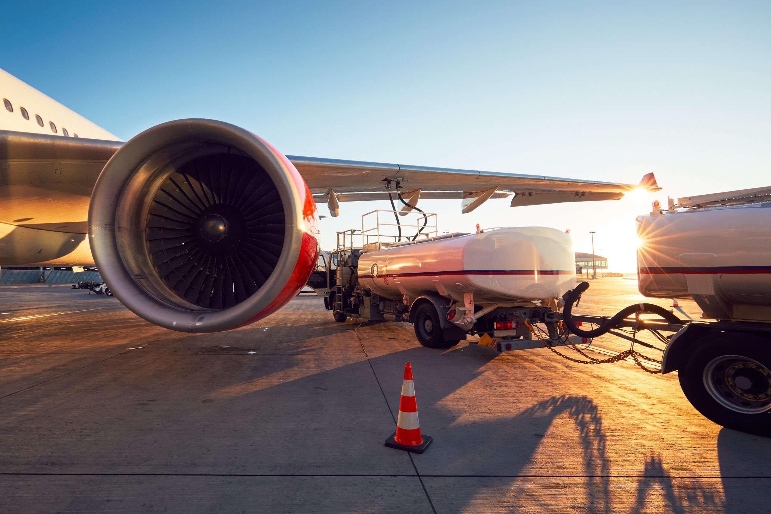 A large jet receiving fuel on an airport runway in front of a bright sunset.