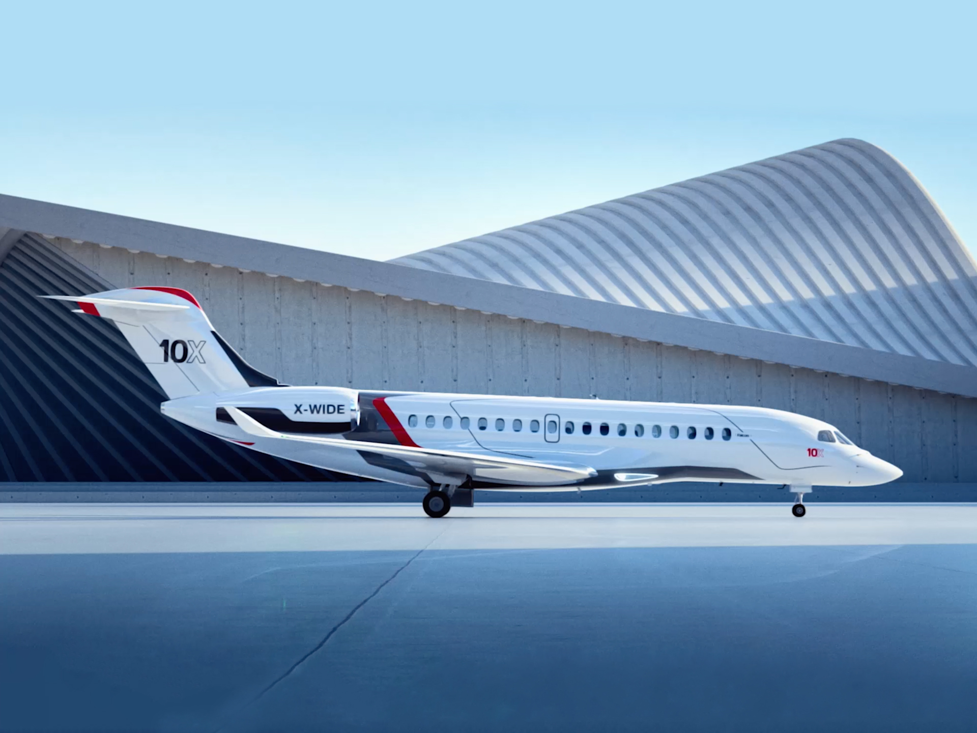 A white Dassault Falcon 10X jet with a black and red stripe. The jet is sat on white concrete in front of a metal building.