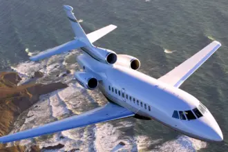 A Dassault Falcon 900EX jet flying over a rocky coastline, with a choppy sea behind it.