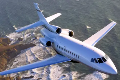 A Dassault Falcon 900EX jet flying over a rocky coastline, with a choppy sea behind it.