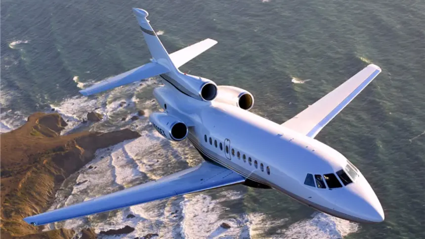 A Dassault Falcon 900EX jet flying over a rocky coastline, with a choppy sea behind it.