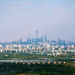 The Beijing skyline behind a dark green field on a cloudy day. The CITIC Tower is clearly visible.
