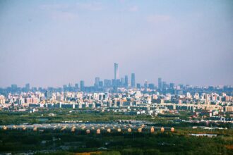 The Beijing skyline behind a dark green field on a cloudy day. The CITIC Tower is clearly visible.