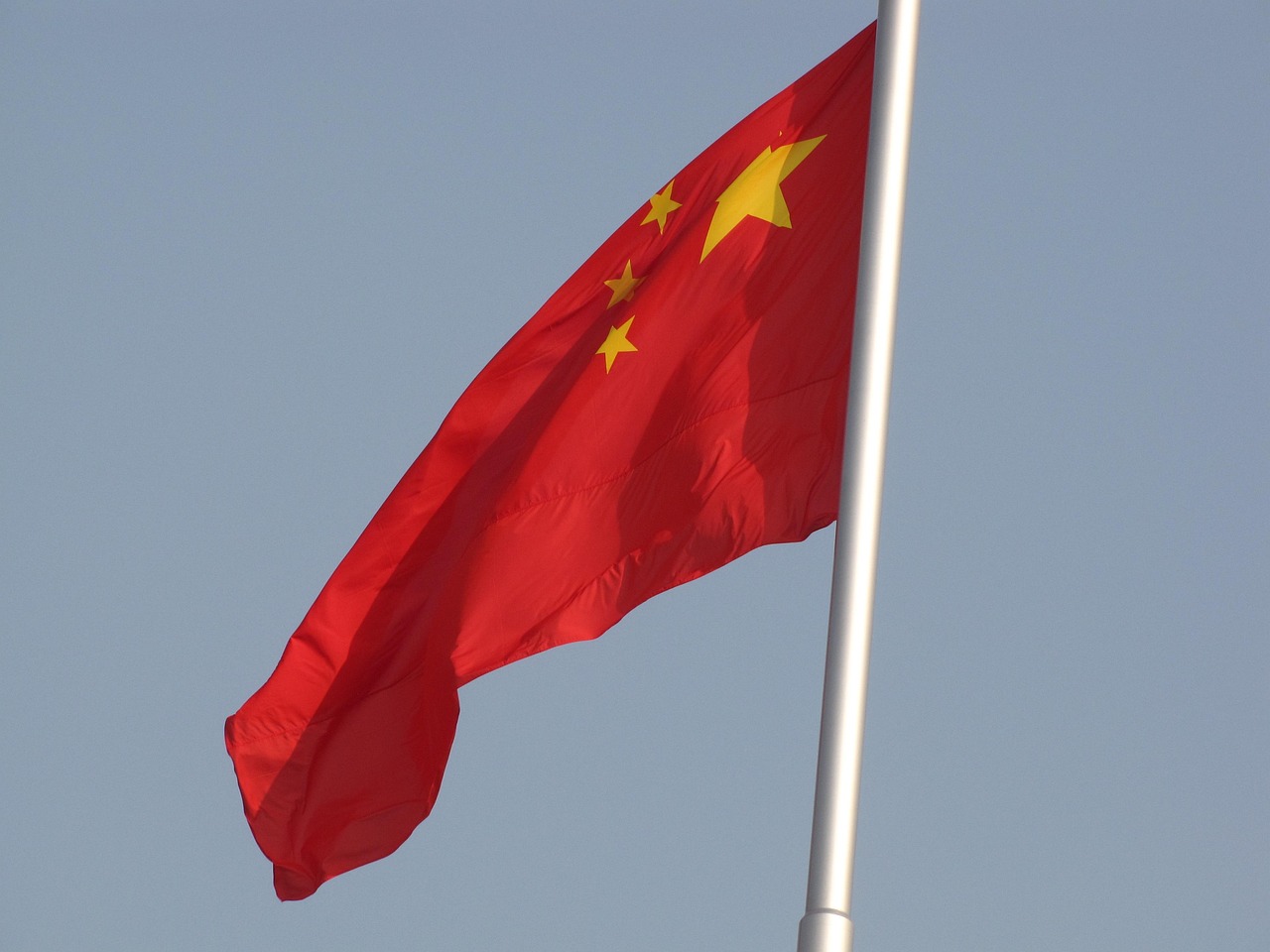 A Chinese national flag flying in front of a grey sky.