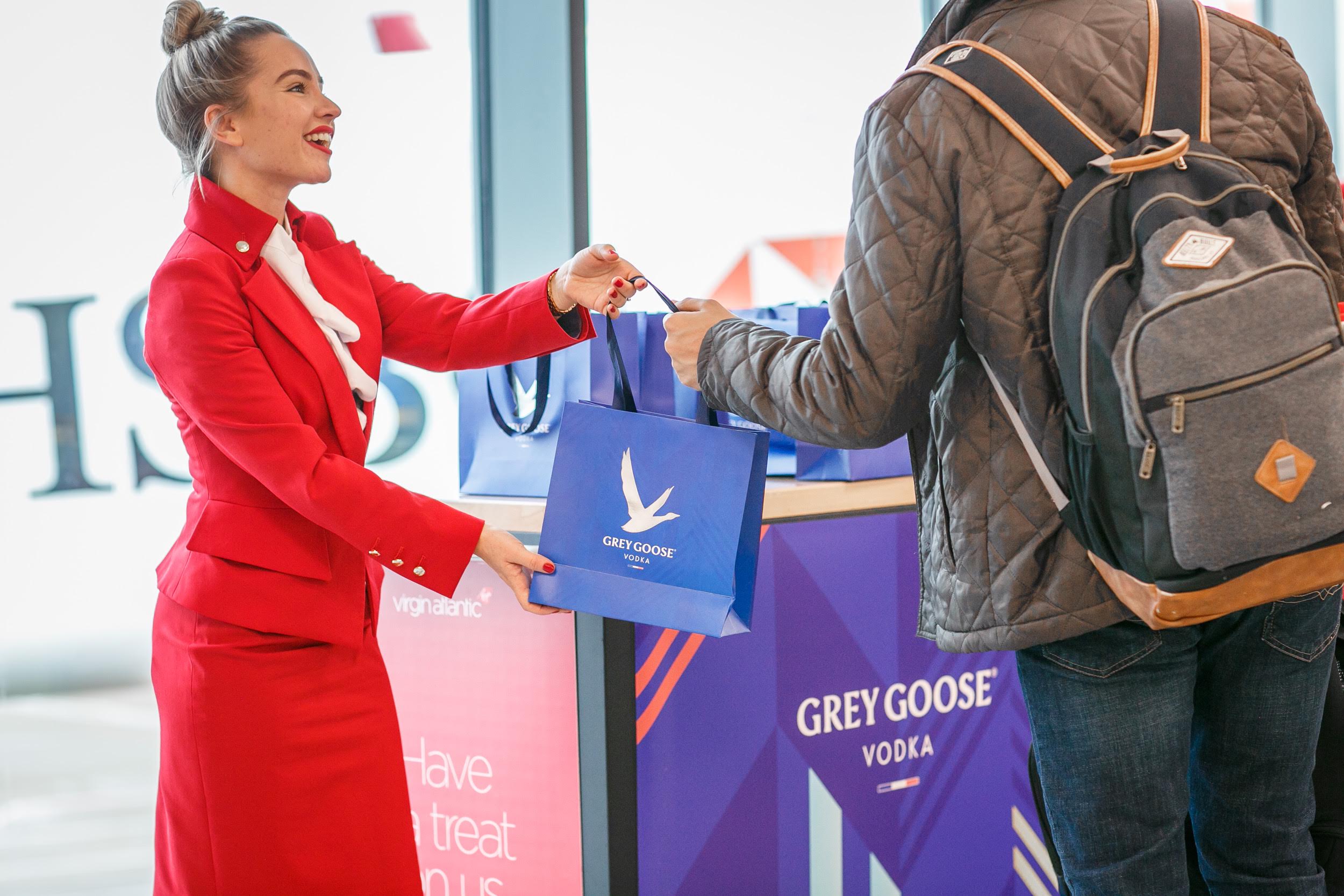 a virgin Atlantic flight attendant handing out bags labelled with Grey Goose vodka to a passenger.