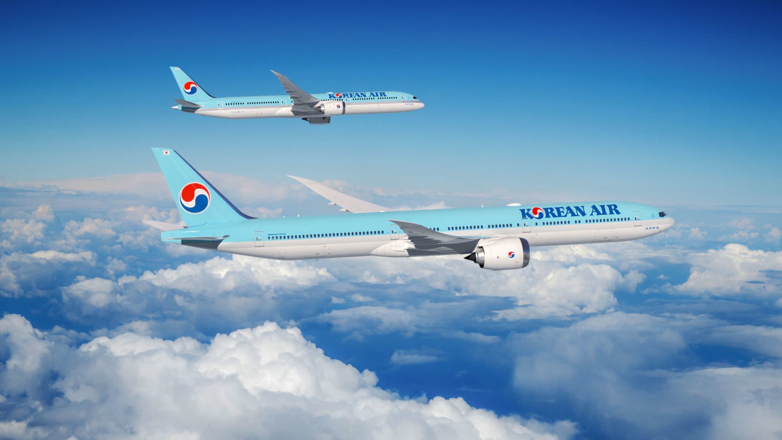 Two Korean Air Boeing Dreamliners flying side by side above the clouds against a blue sky