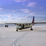 This image shows a Britten-Norman BN-2 Islander aircraft operated by Loganair (sporting a British Airways Express livery) sitting on the snow-covered Fair Isle airstrip in Shetland, Scotland.