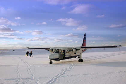 This image shows a Britten-Norman BN-2 Islander aircraft operated by Loganair (sporting a British Airways Express livery) sitting on the snow-covered Fair Isle airstrip in Shetland, Scotland.
