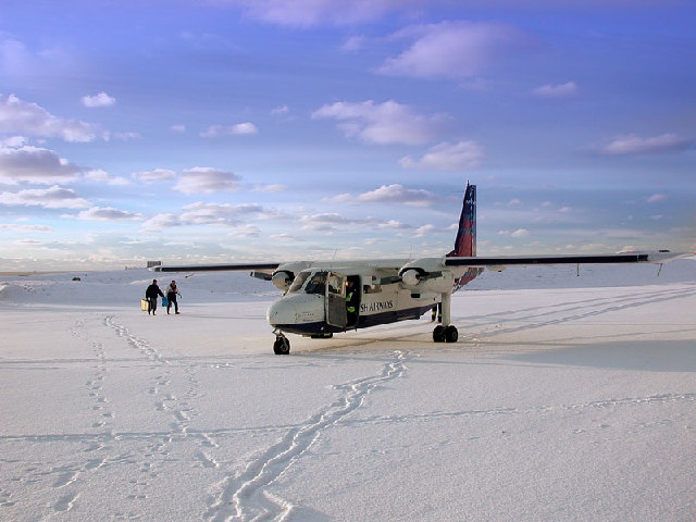 This image shows a Britten-Norman BN-2 Islander aircraft operated by Loganair (sporting a British Airways Express livery) sitting on the snow-covered Fair Isle airstrip in Shetland, Scotland.