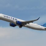 A United Airlines Airbus A321neo is pictured climbing through a cloudy blue sky after take-off.