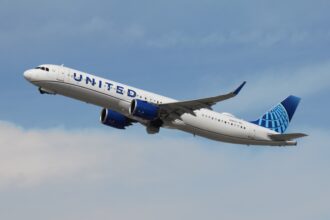 A United Airlines Airbus A321neo is pictured climbing through a cloudy blue sky after take-off.