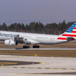 An American Airlines Airbus A330-243 aircraft taking off from the runway. Trees and a grey/blue sky in the background.
